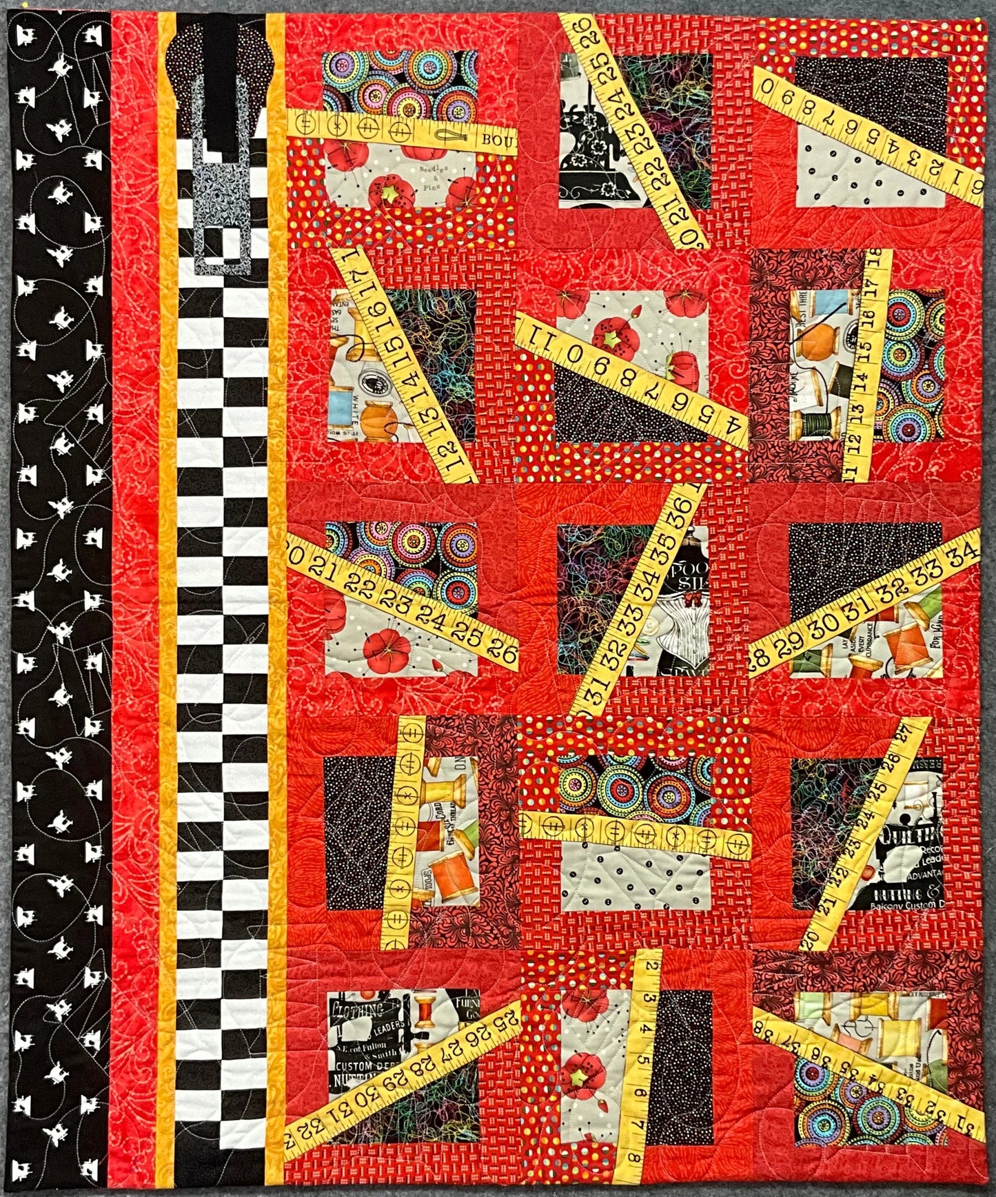 Sew n Stuff: Quilted Wall Art by Mary Cantore features bold red squares, patterned borders, diagonal yellow measuring tape strips, and black-and-white stripes—a striking décor piece for any sewing enthusiasts room.