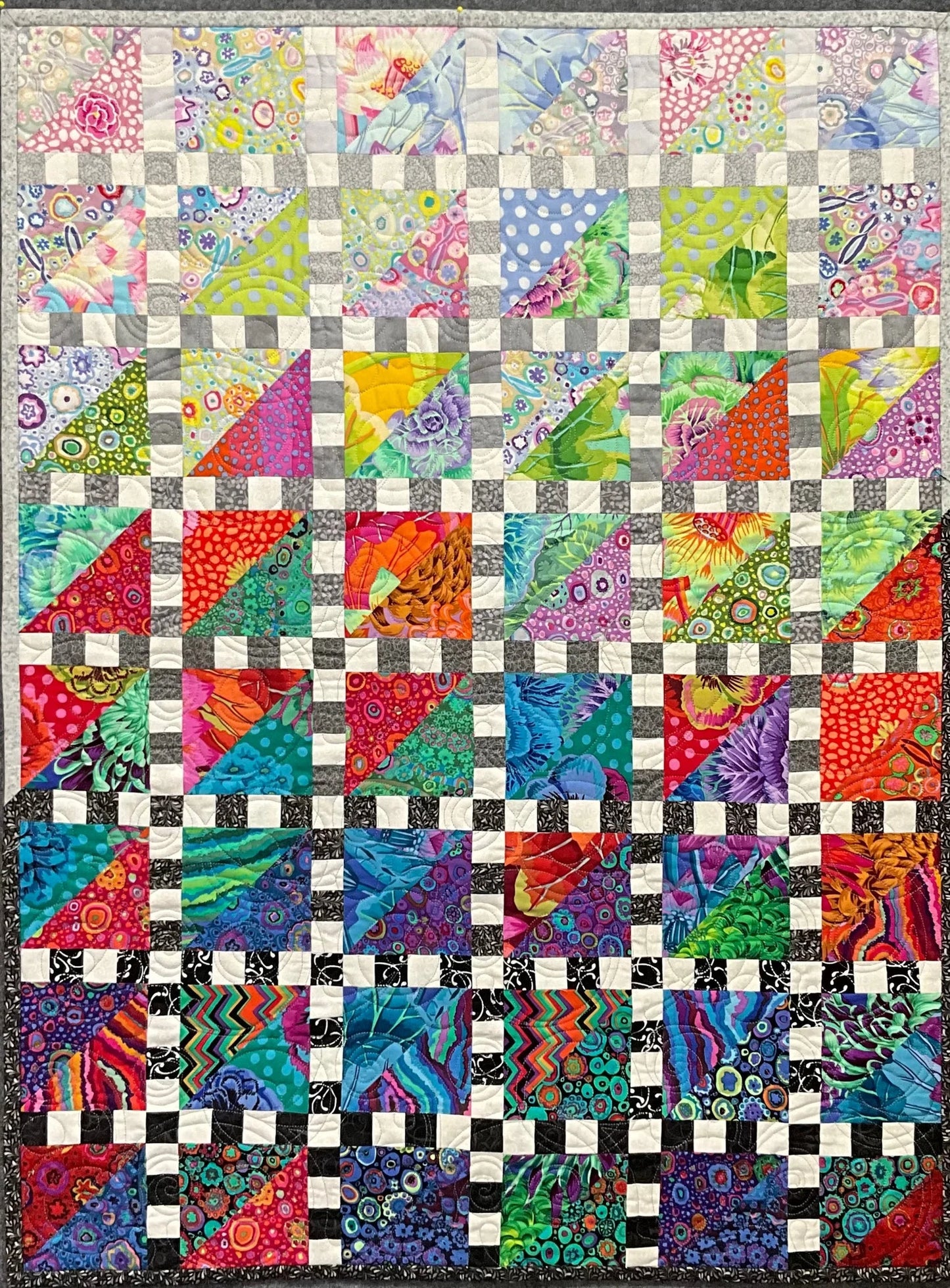 Mary Cantore’s Walking the Rainbow: Quilted Wall Art features colorful geometric and floral triangles and squares in red, blue, green, purple, and yellow, with small white squares creating a striking grid—an eye-catching home decor piece.