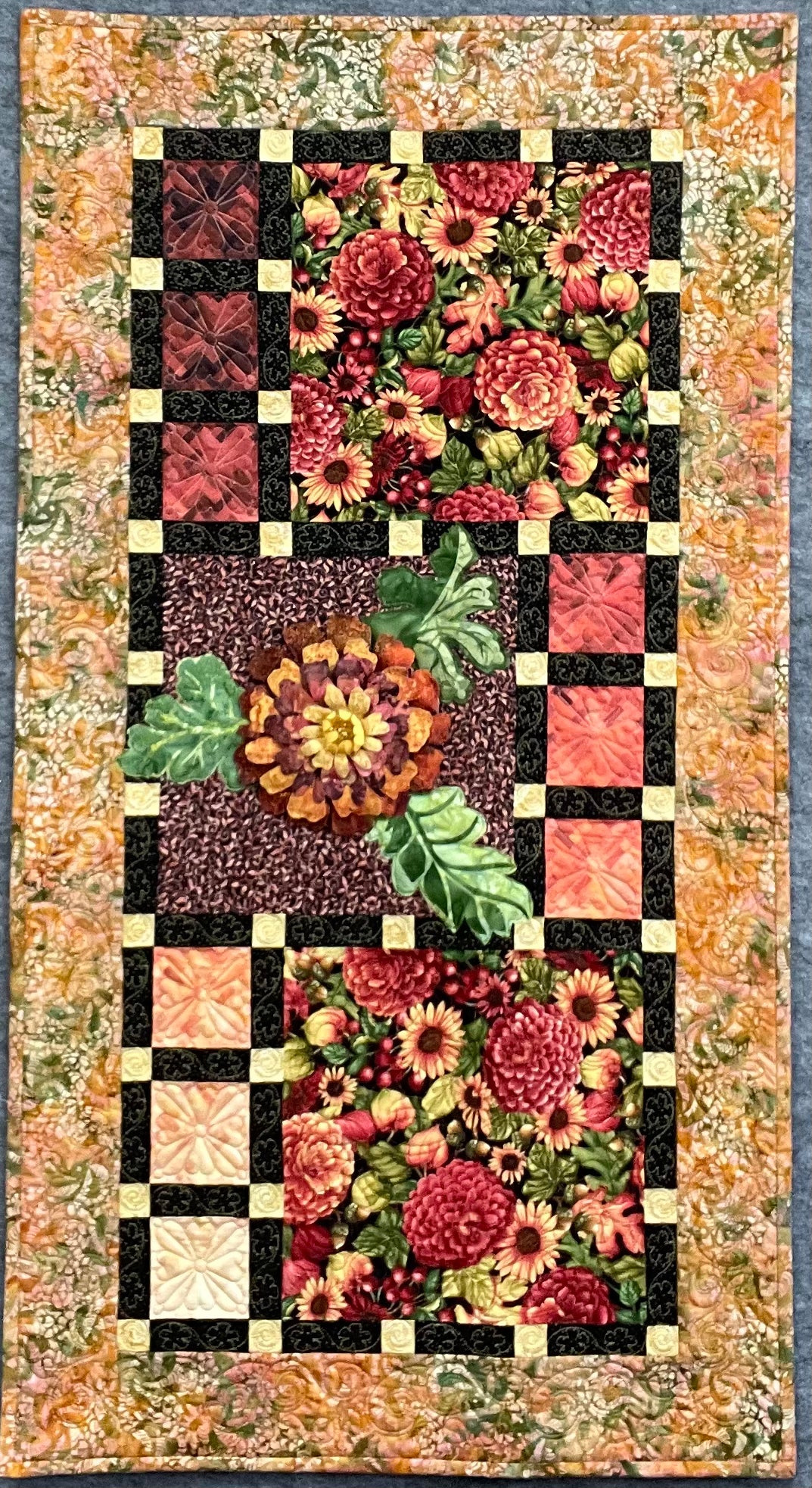 The Grand Finale: Quilted Wall Art by Mary Cantore is a rectangular quilt with bright red, orange, yellow, and green florals, bordered by variegated strips and checkerboard patchwork—perfect for vibrant fall decor.