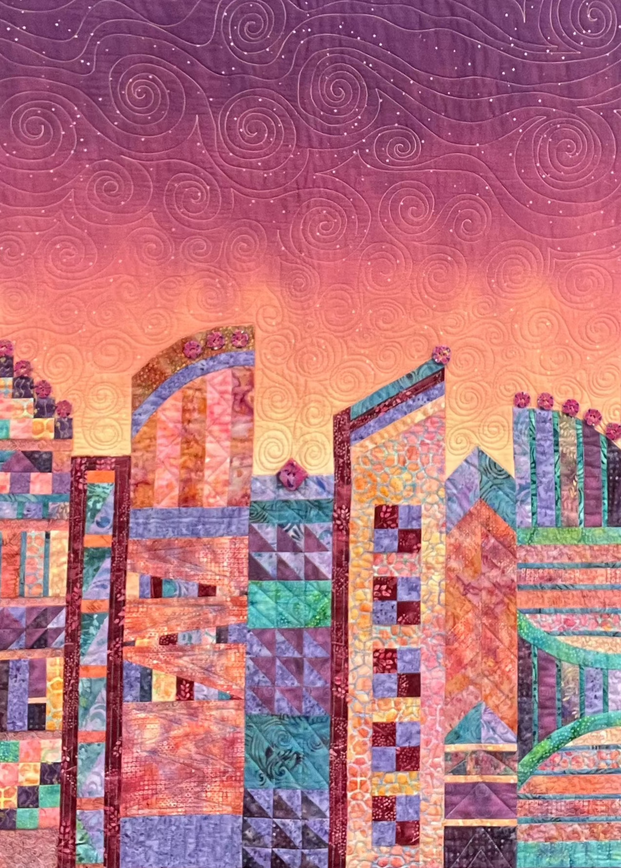 Mary Cantores Purple Twilight: Quilted Wall Art features abstract city buildings beneath a vibrant, swirling purple and orange sunset, with intricate stitched patterns enhancing the lively cityscape.