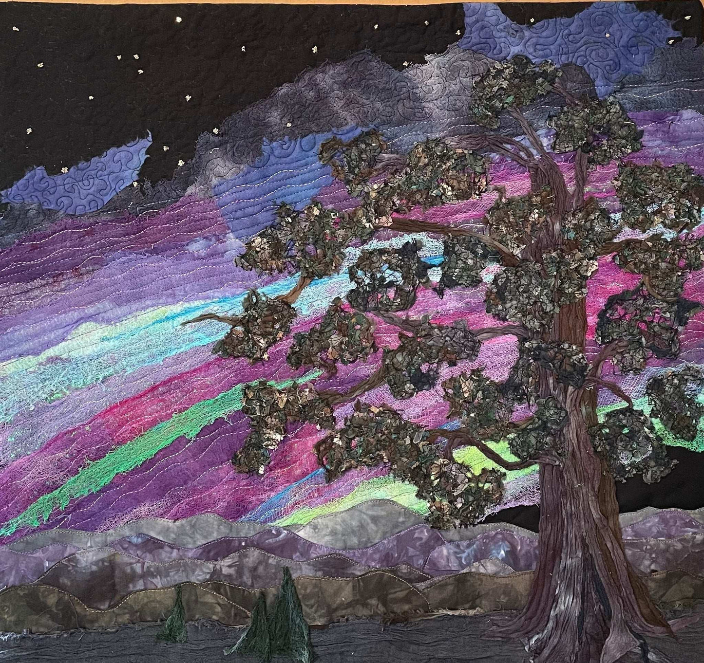 The Aurora Borealis: Landscape Art Quilt by Miki Howell features a handcrafted textured tree under a starry sky illuminated with vibrant pink, purple, and green tones above distant mountains—a stunning textile wall hanging.