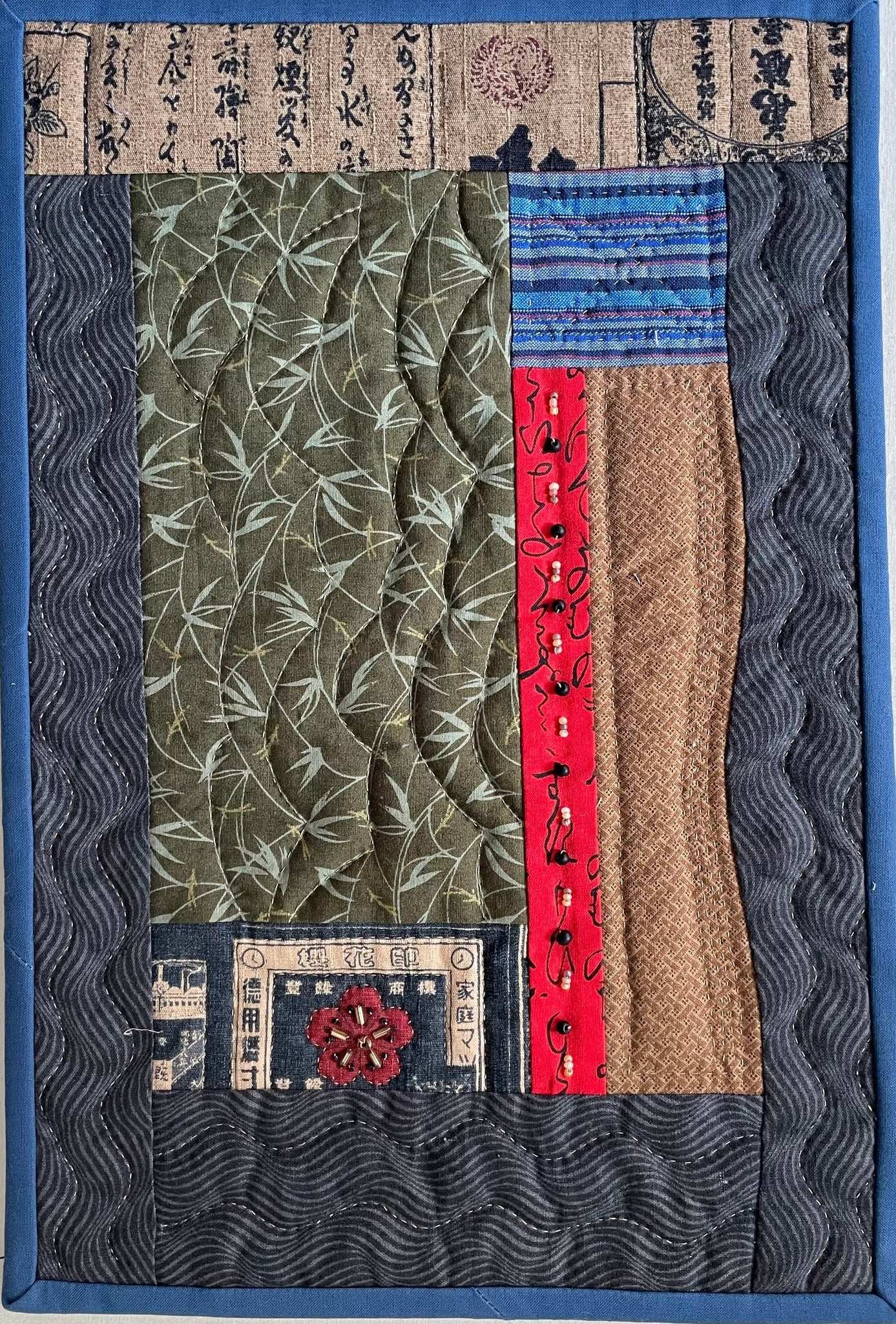 Memories of Japan: Art Quilt by Miki Howell is a cotton wall quilt with green, red, brown, and blue rectangles, Japanese text prints, wavy lines, a red flower accent, and a dark wavy-patterned border.