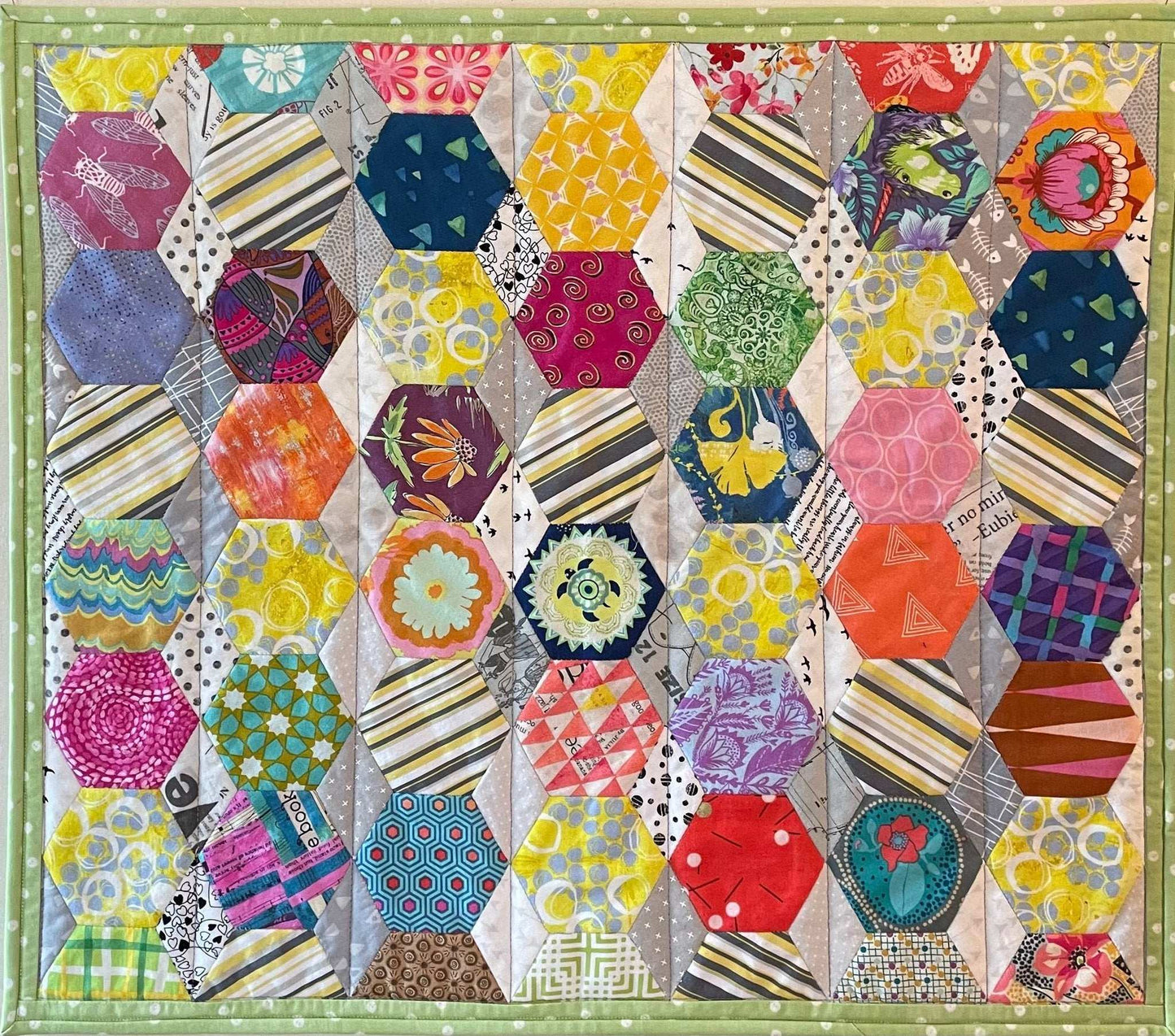 Hexi Fun: Art Quilt by Miki Howell is a colorful wallhanging with octagons, diamonds, and Hexi Fun patterns in vibrant yellow, pink, blue, green, and orange shades, bordered by light green fabric using English paper piecing.