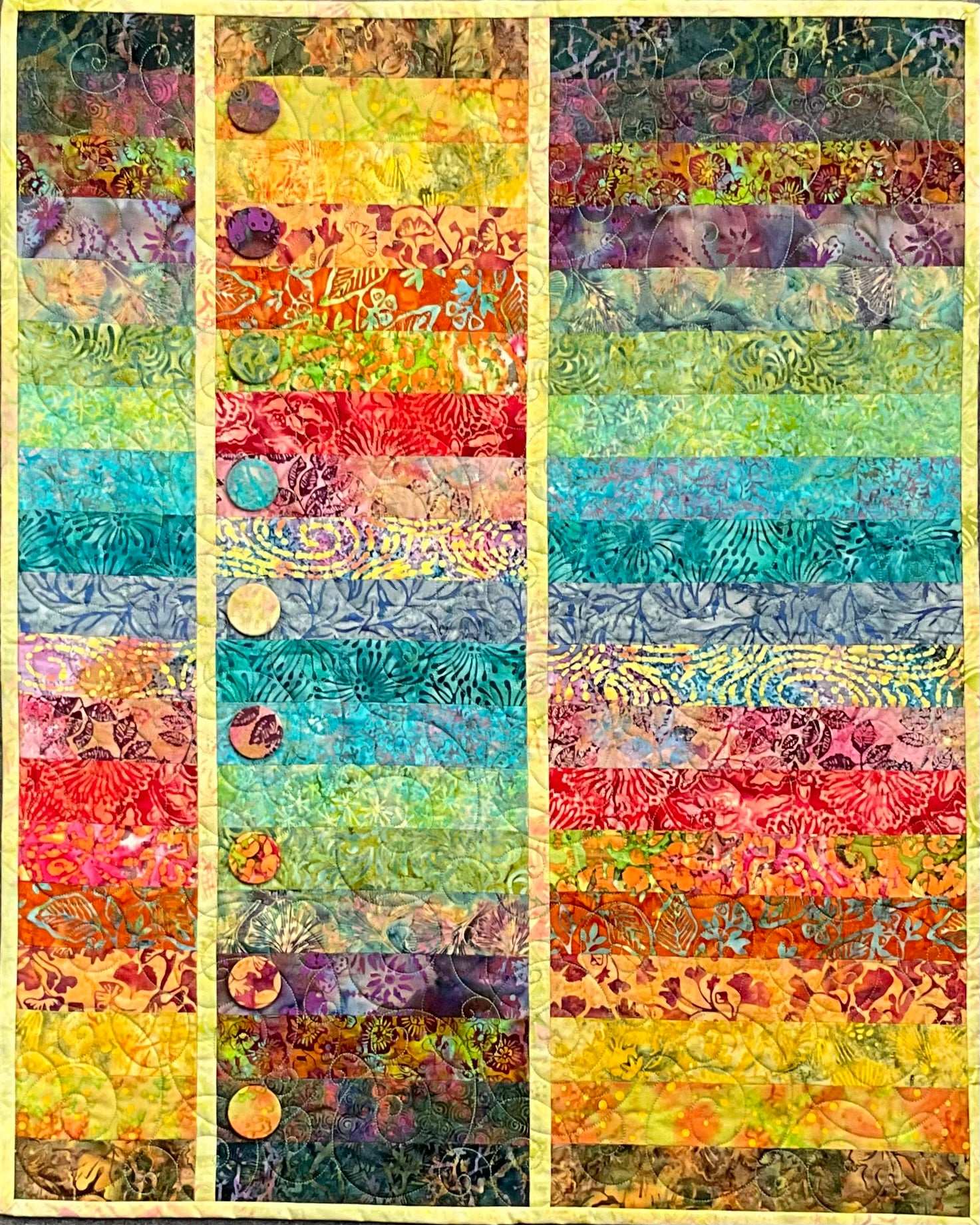 Topsy Turvy: Quilted Wall Art by Mary Cantore showcases vibrant batik strips—yellow, orange, red, green, blue, and purple—with three beige sashing stripes and circular appliques on the left panel. A striking piece for home decor.