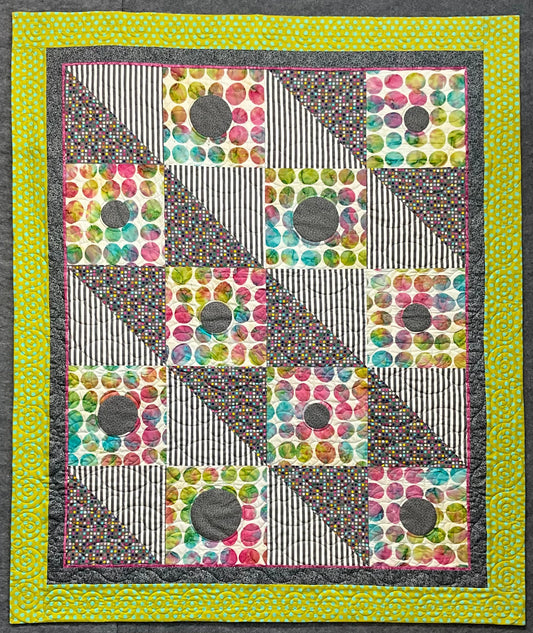 The Seeing Spots: Quilted Wall Art by Mary Cantore features colorful, diagonally divided squares with polka dot, striped, and spotted patterns, gray circular patches, a yellow-green border, and a purple stripe—perfect for a child’s room.
