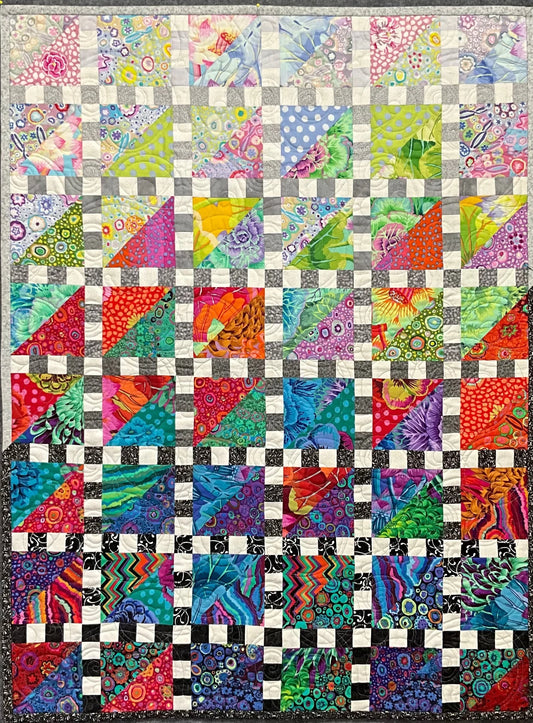 Mary Cantore’s Walking the Rainbow: Quilted Wall Art features colorful geometric and floral triangles and squares in red, blue, green, purple, and yellow, with small white squares creating a striking grid—an eye-catching home decor piece.