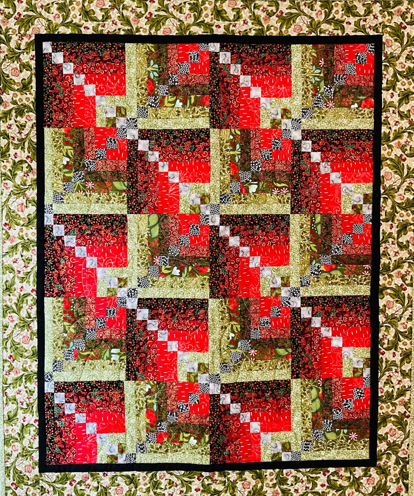 Holiday Spice: Quilted Wall Art by Mary Cantore features a log cabin patchwork in festive colors, bordered with floral fabric and a black frame—perfect as cozy holiday decor or to add seasonal charm to any room.