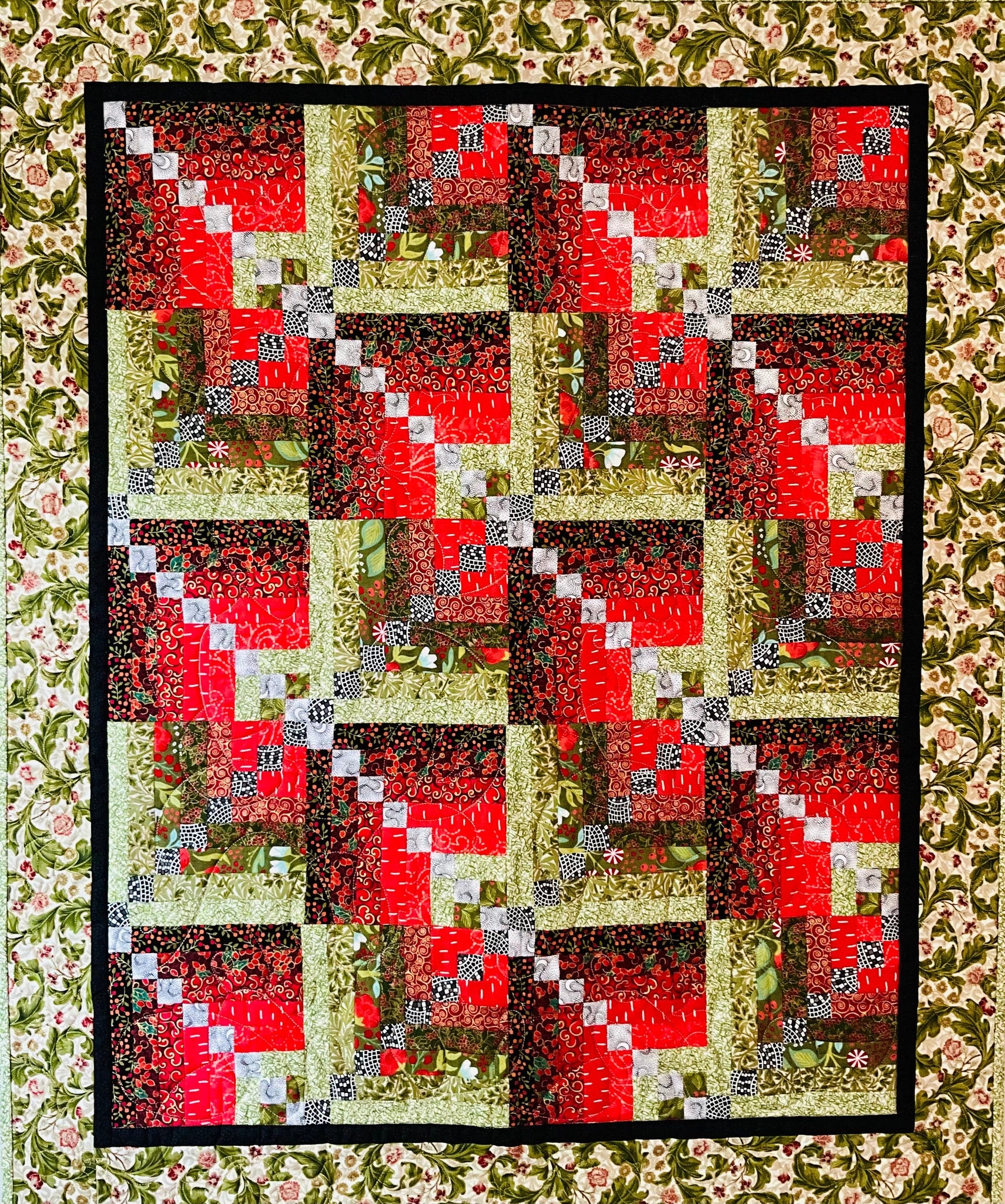 Holiday Spice: Quilted Wall Art by Mary Cantore features a log cabin patchwork in festive colors, bordered with floral fabric and a black frame—perfect as cozy holiday decor or to add seasonal charm to any room.
