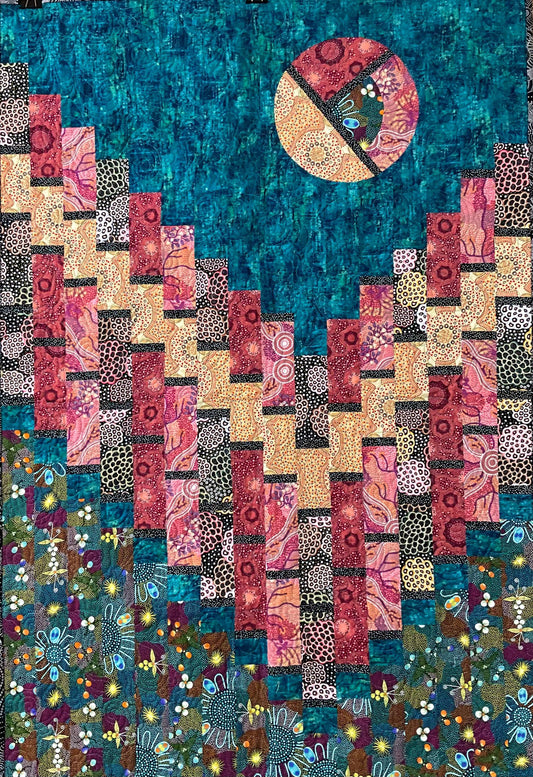 Moon Over Magdalaina: Quilted Wall Art by Mary Cantore features a vibrant sun in a teal sky above patterned pink, yellow, and red blocks resembling the Australian outback, with a floral design accenting the bottom.