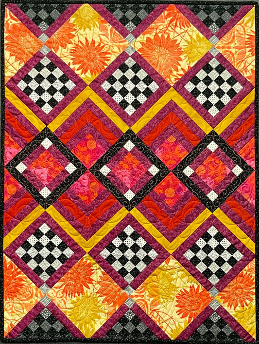 The Morocco: Quilted Wall Art by Mary Cantore features a diamond pattern with checkerboard squares and vibrant red, yellow, orange, and pink florals, bordered by black, yellow, and magenta strips—perfect for unique home decor.