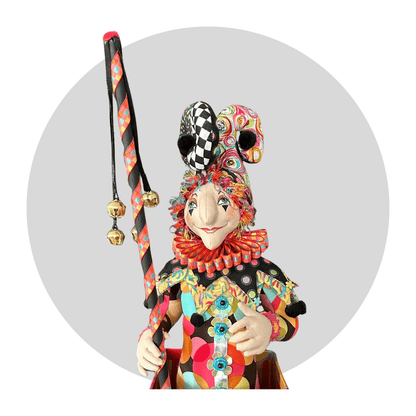 Jack Jack itb: An Art Doll by Mary Cantore is a whimsical jester with a patterned suit, ruffled collar, playful hat, and ribbon-adorned staff, shown against a plain gray circular background.