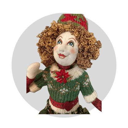 Noelle: Art Doll by Mary Cantore features curly hair, a green and white knit sweater, red and green hat, and a red flower on the chest, smiling upward against a light gray circular background.