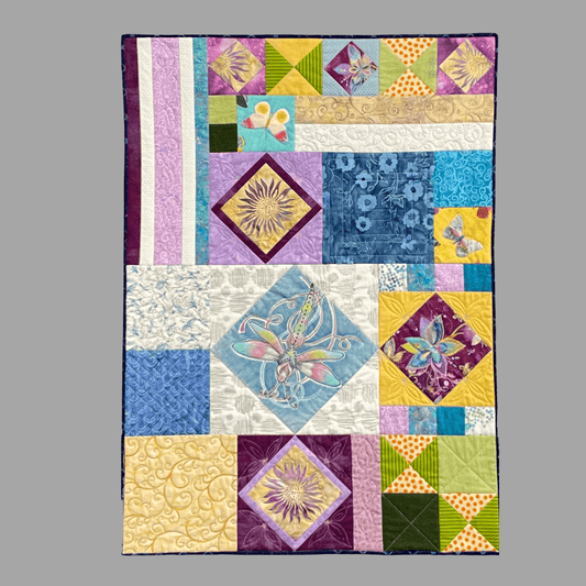 The Sunshine on the Wings: Art Quilt by Miki Howell features geometric and floral patterns, butterfly and dragonfly motifs in purple, blue, yellow, green, and pink on a solid grey background.